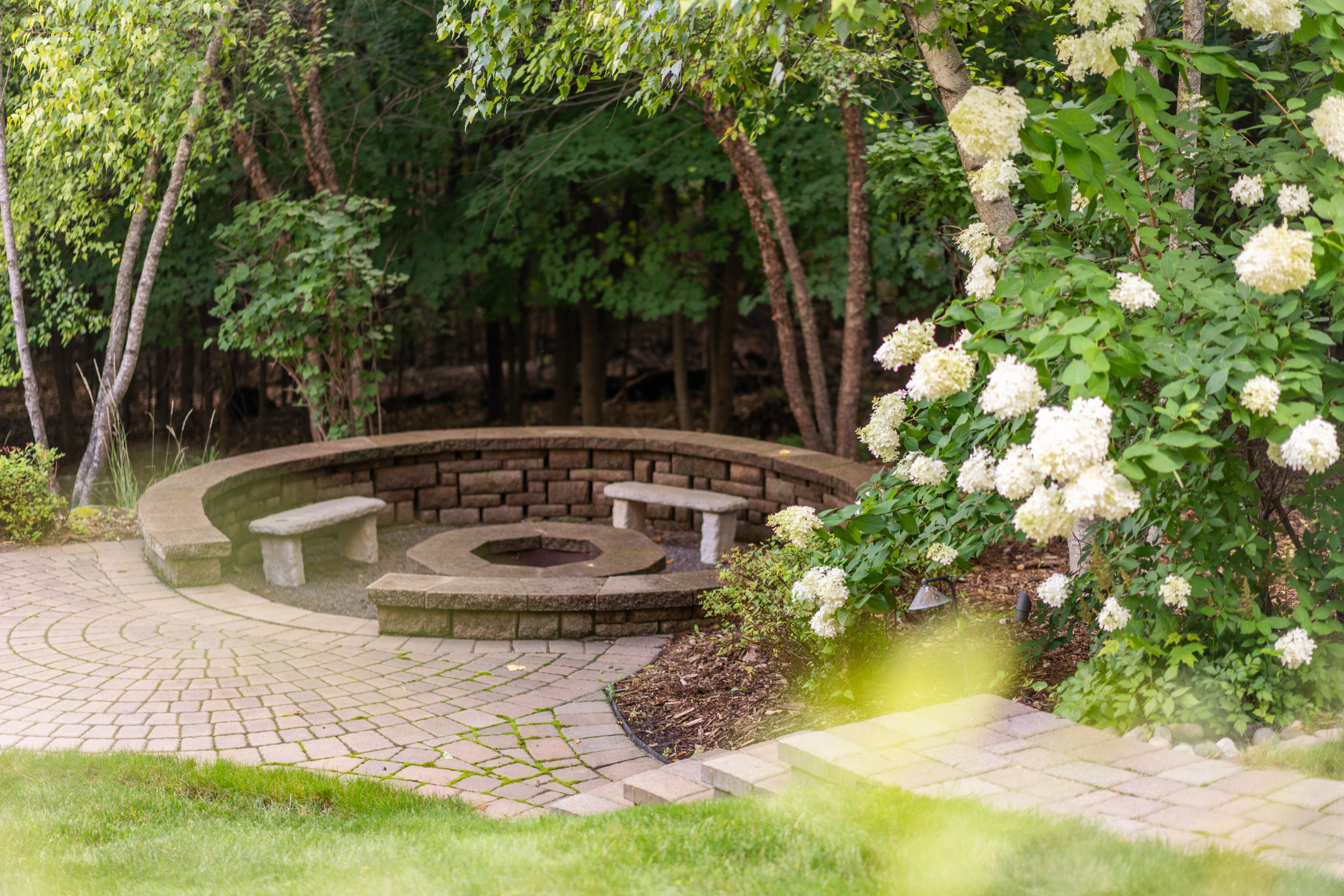 Stone fire pit seating area in lush garden, real estate photography for personal brand.
