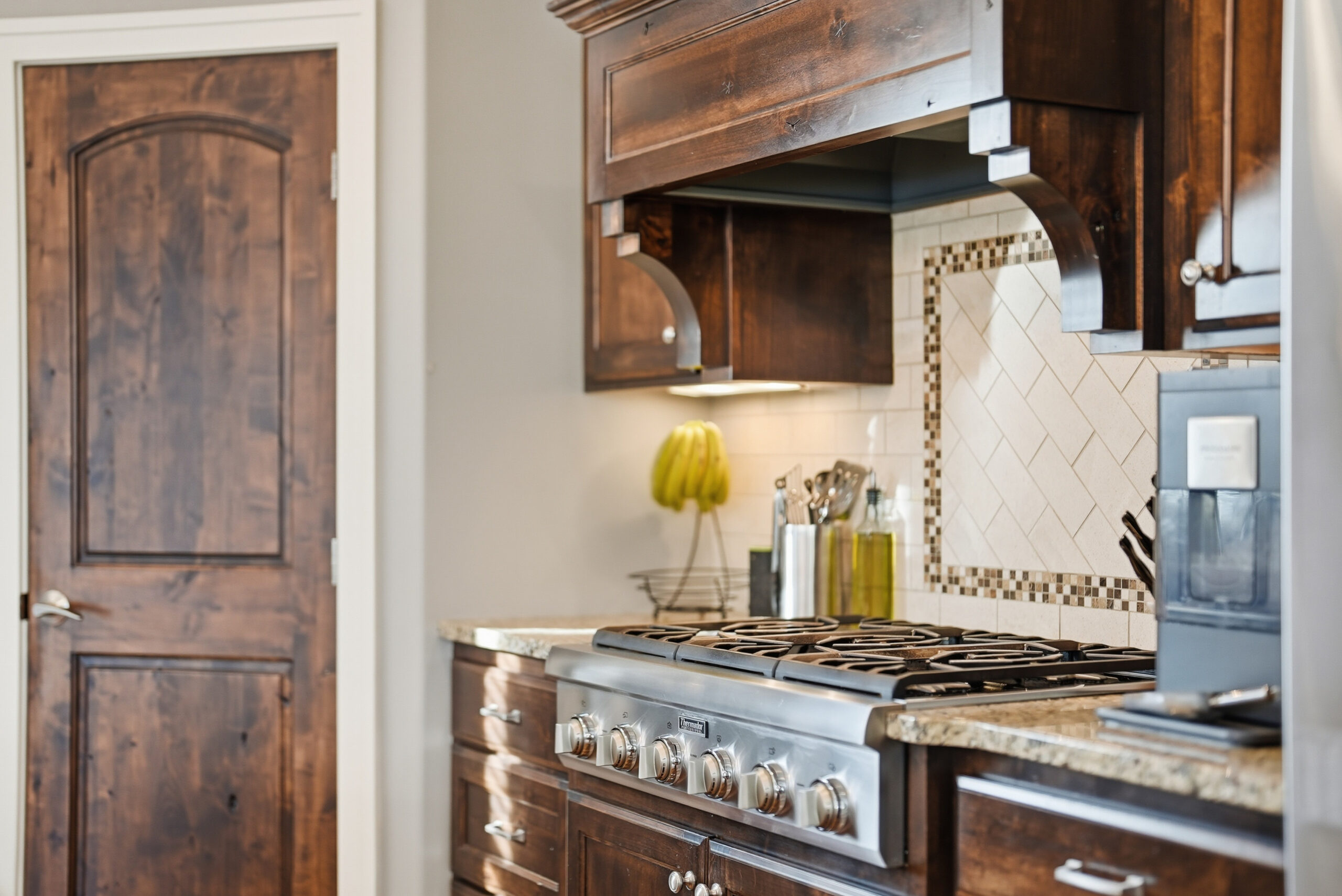 Real estate photography showcasing kitchen with stainless steel appliances and wood cabinetry.