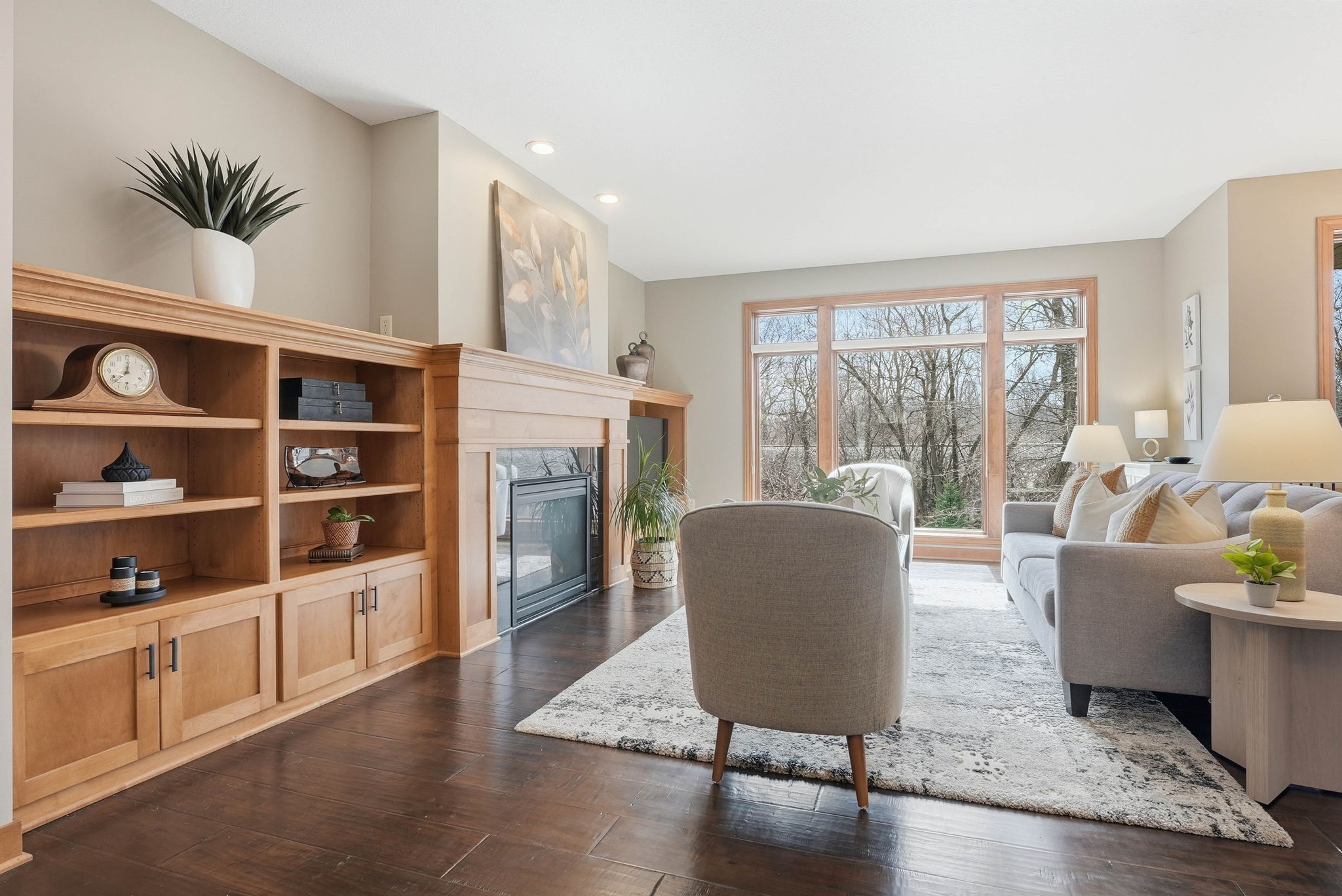 Walkout rambler living room with fireplace, built-in bookshelves, and large windows overlooking trees.