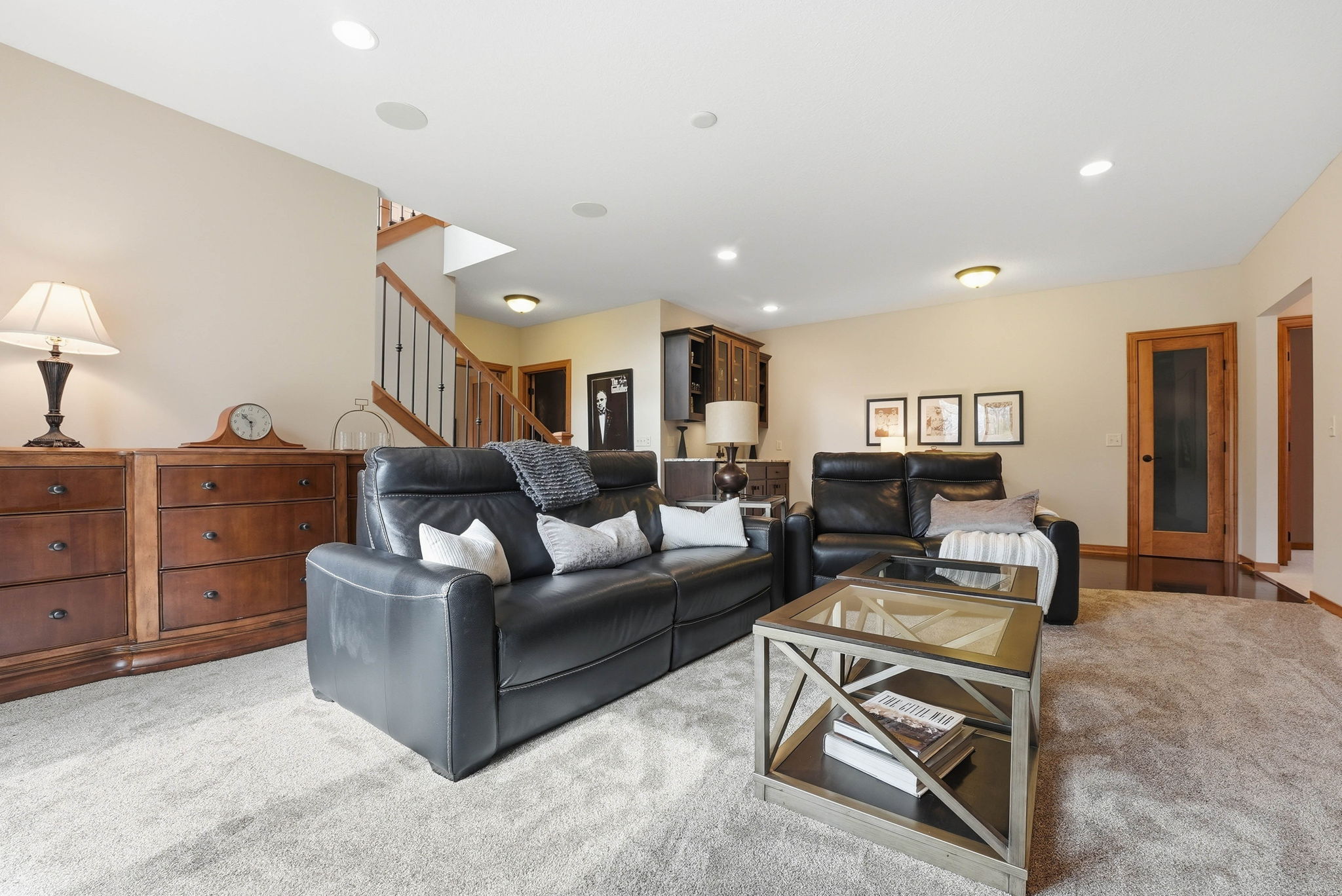 Walkout rambler interior with leather recliners, wood cabinetry, and staircase.