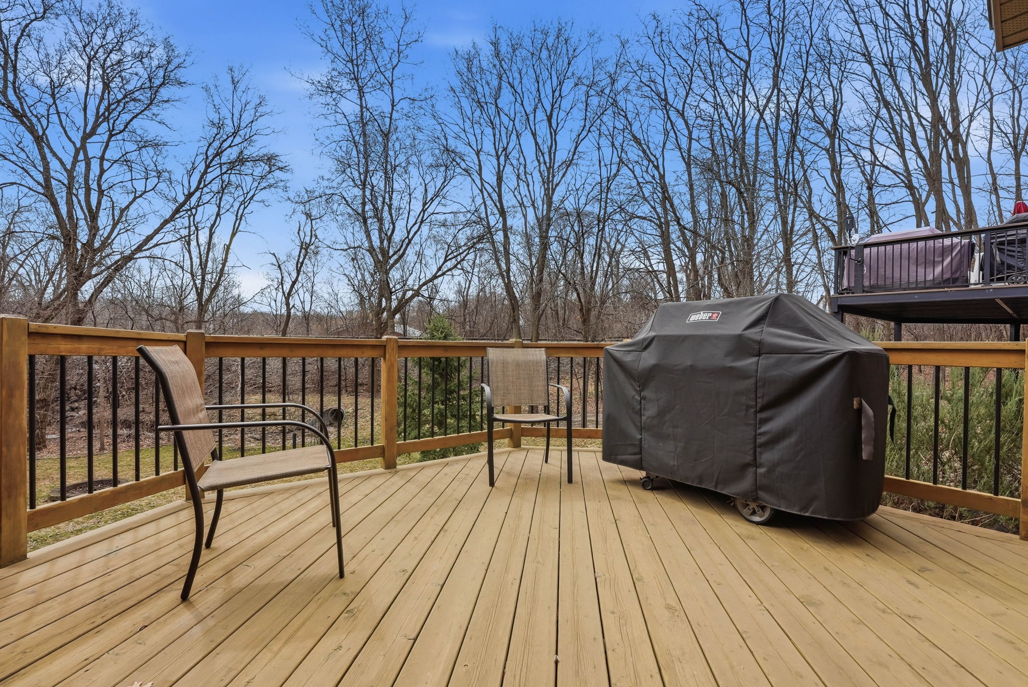 Expanded deck overlooking private backyard with grill and patio furniture.